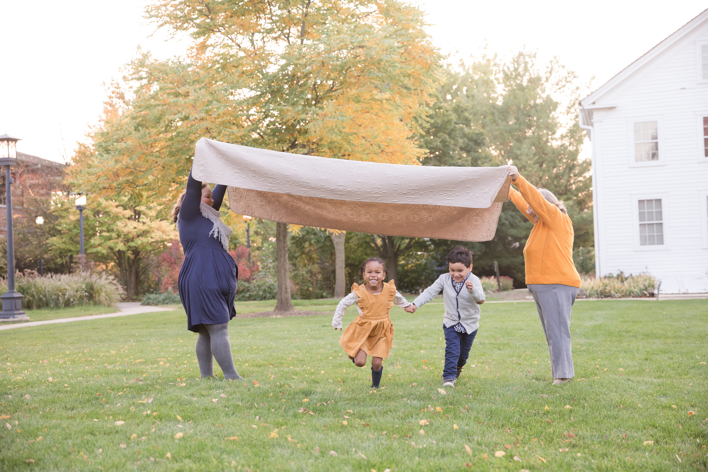 parents holding blanket above kids as they run underneath it